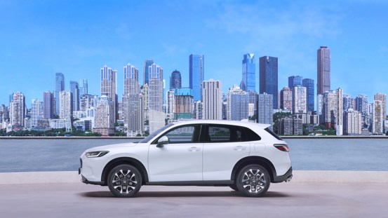 Honda ZR-V full hybrid SUV side view in Diamond Dust Pearl, with skyscrapers and glass buildings in the background.