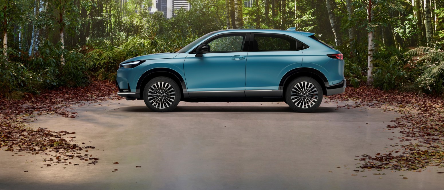 Honda full electric car e:Ny1 in Aqua Topaz Metallic surrounded by trees and skyscrapers views.