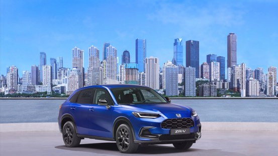 Honda ZR-V full hybrid SUV in Still Night Pearl, parked on a city street with skyscrapers in the background.