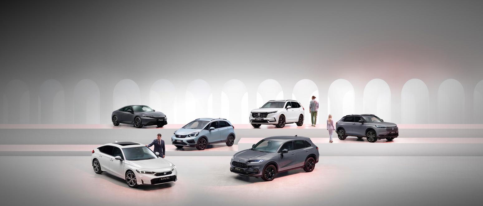 Six Honda vehicles are shown in a sleek, minimalistic showroom with people standing near some of the cars.
